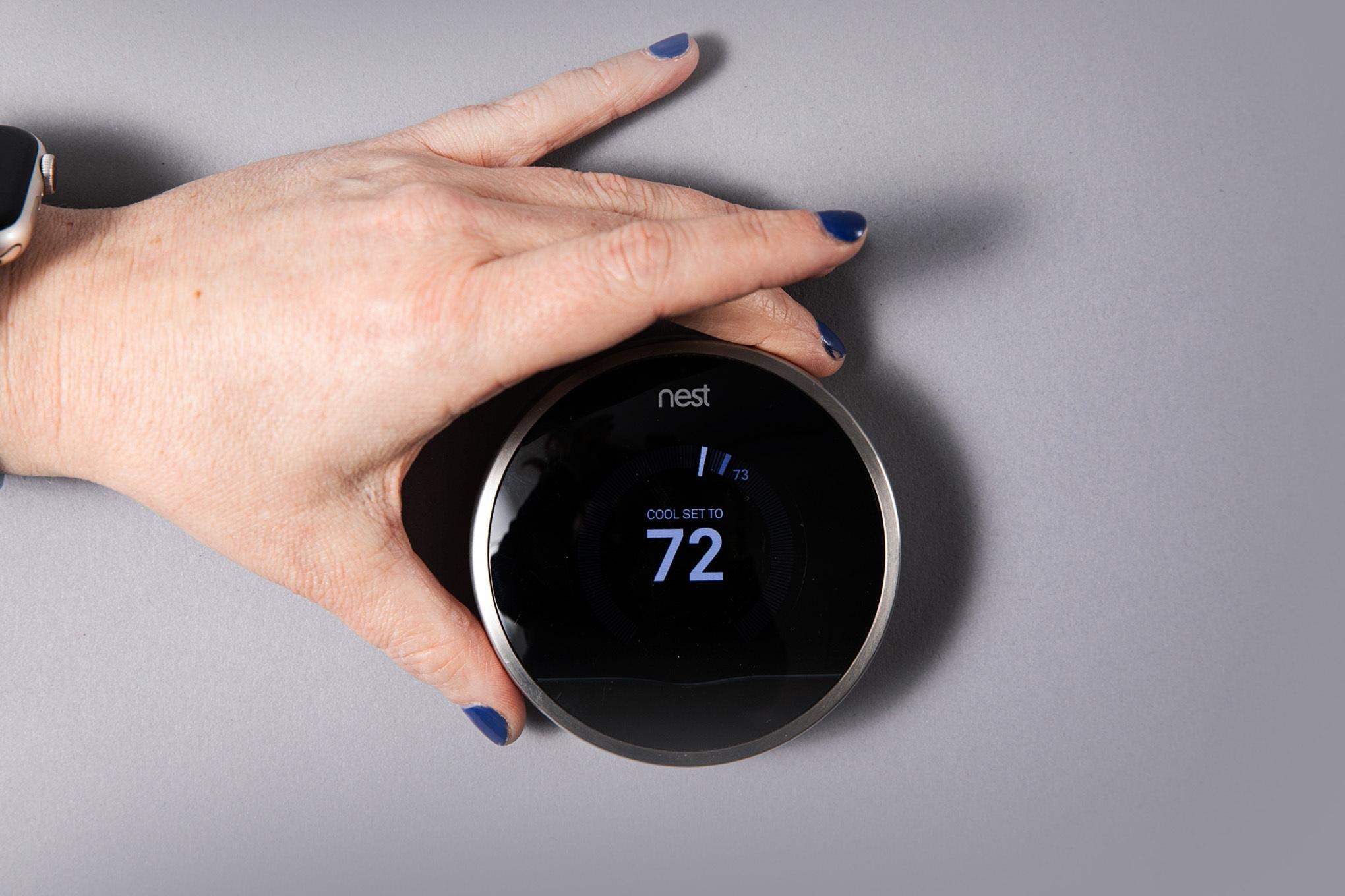 A photo of a hand reaching out to turn a thermostat up.