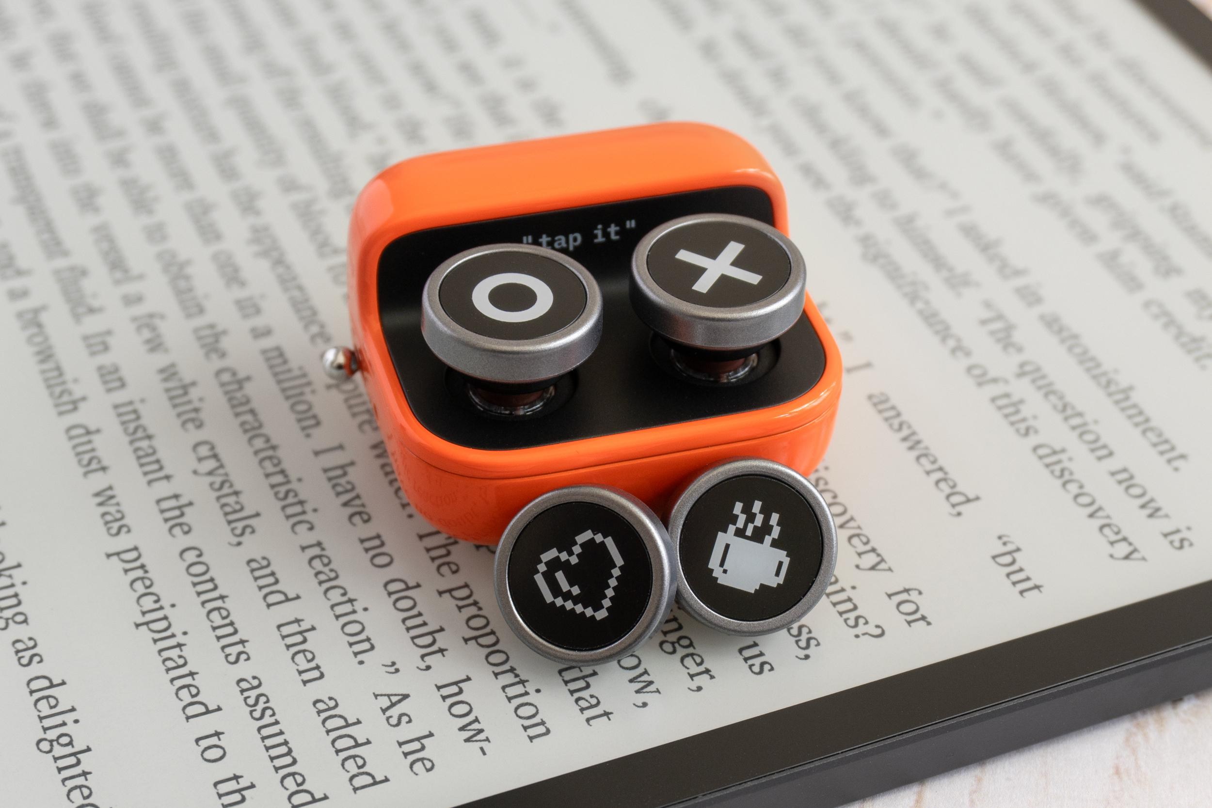 The Boox Tappy on an e-reader next to the included alternate button designs. The Boox Tappy on an e-reader next to the included alternate button designs.