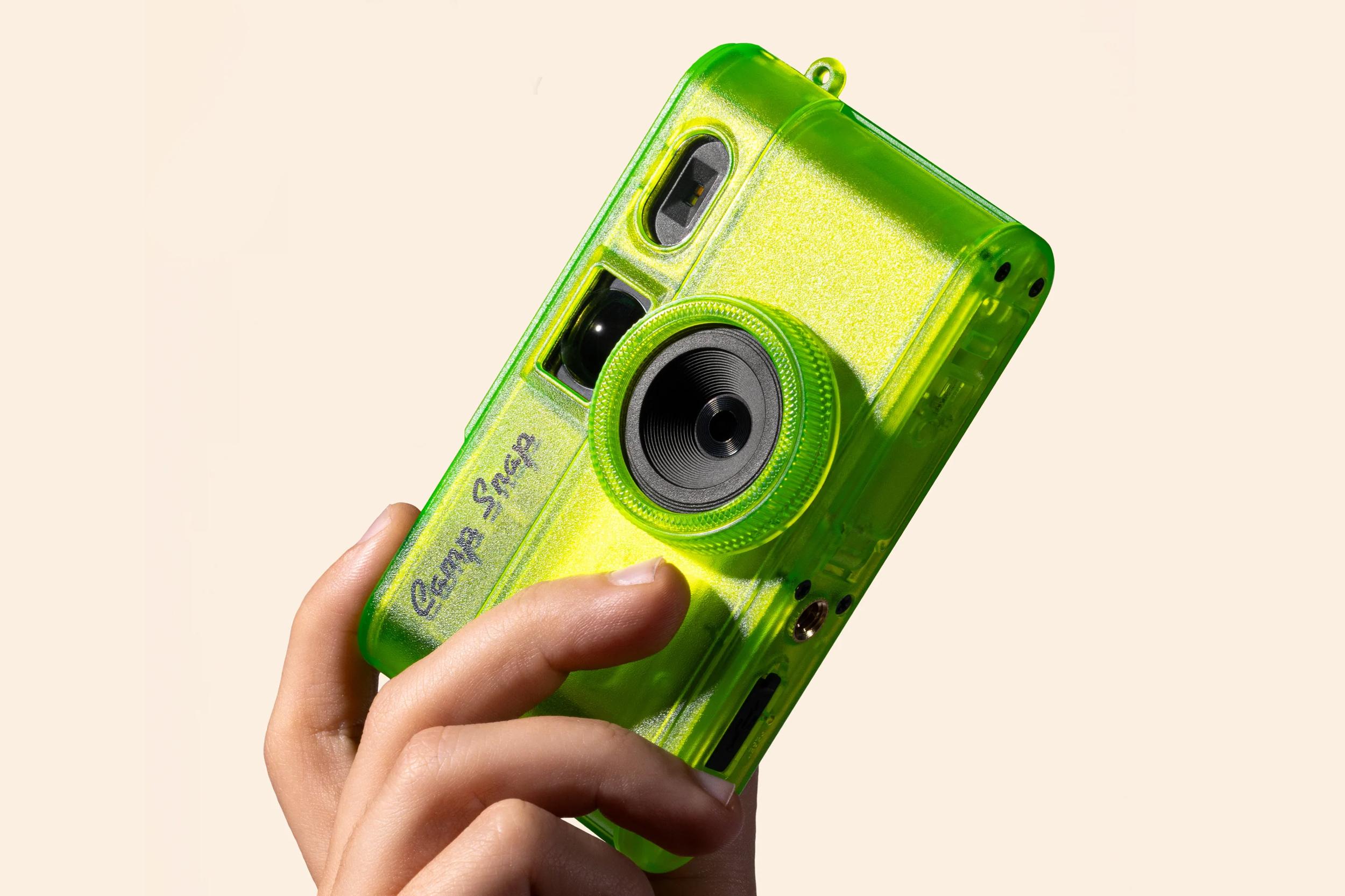 A hand holding a transparent green version of the Camp Snap 2 camera.