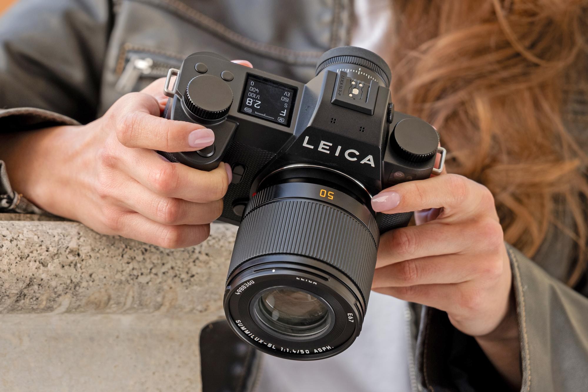 A person holds the Leica SL3-P camera in two hands while looking at its rear LCD display.