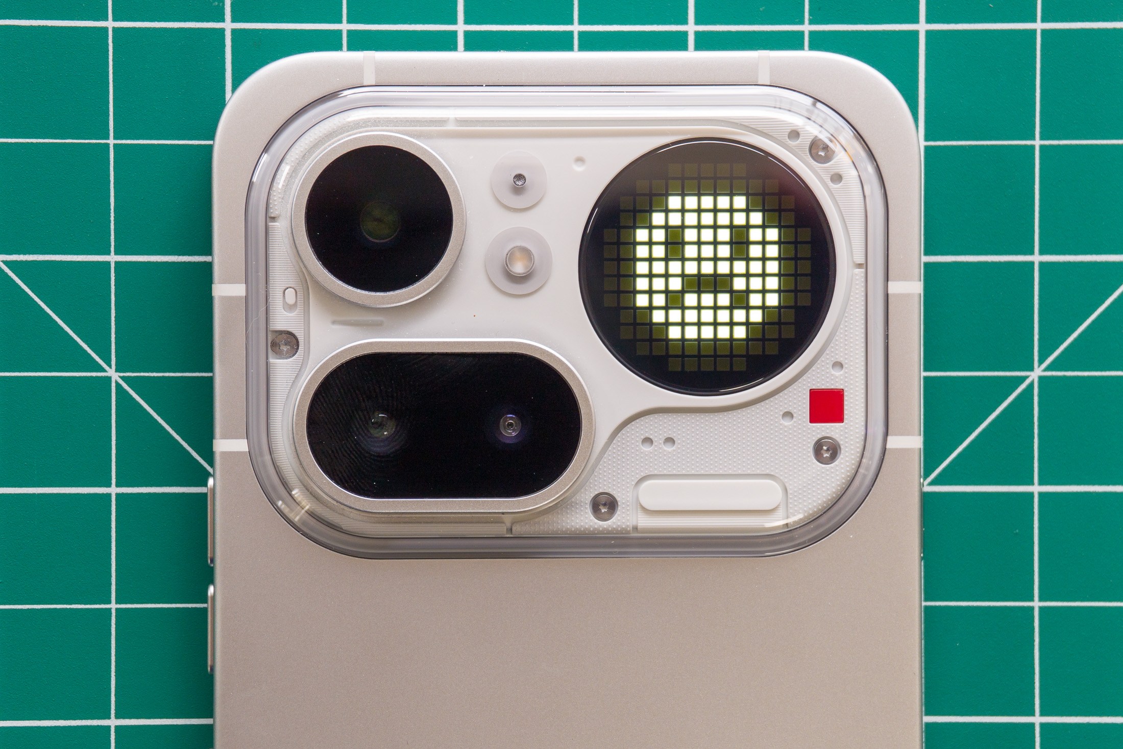 Photo of Nothing Phone 4A Pro on a green cutting mat showing the camera module with an unhappy smiley face on the Glyph Matrix