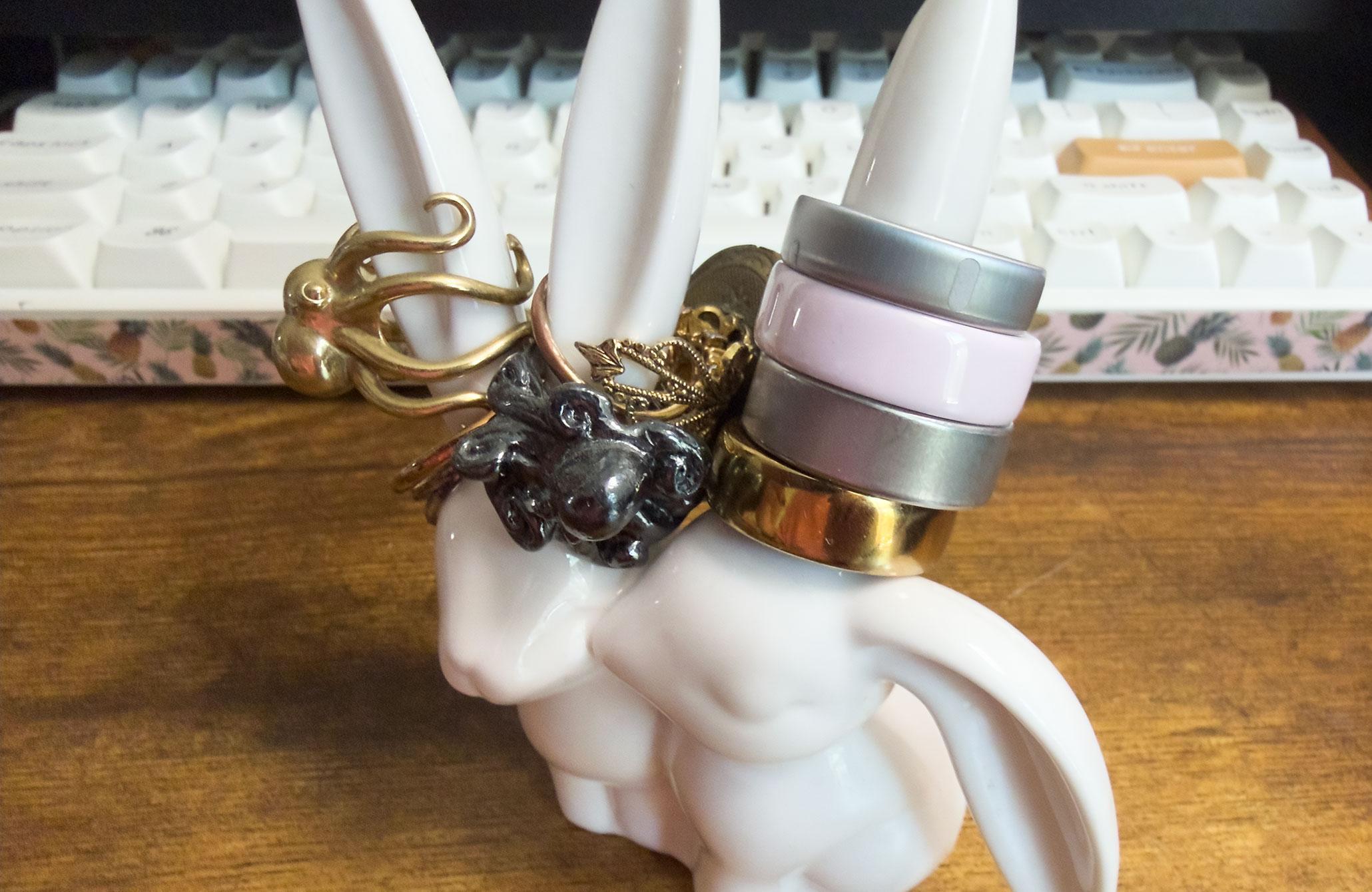 A ring stand shaped like two bunnies with four Oura Rings perched on the right-most bunny’s left ear. In order from top to bottom, it is the Oura Ring 5, Oura Ring 4 Ceramic, Oura Ring 4, and Oura Ring Gen 3.