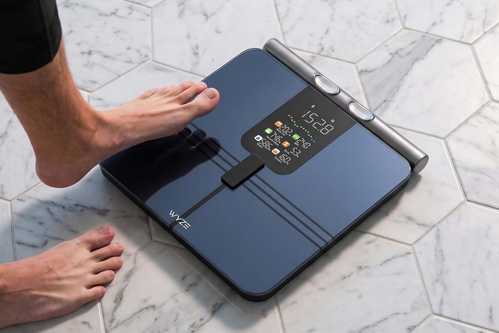 A person steps with one foot on to the Wyze Scale BodyScan placed on a tile floor.