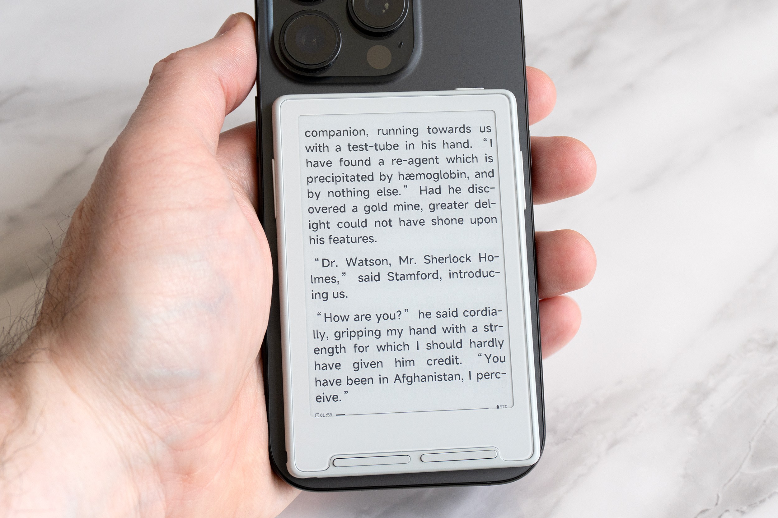 A hand holds the Xteink X3 e-reader attached to an iPhone.
