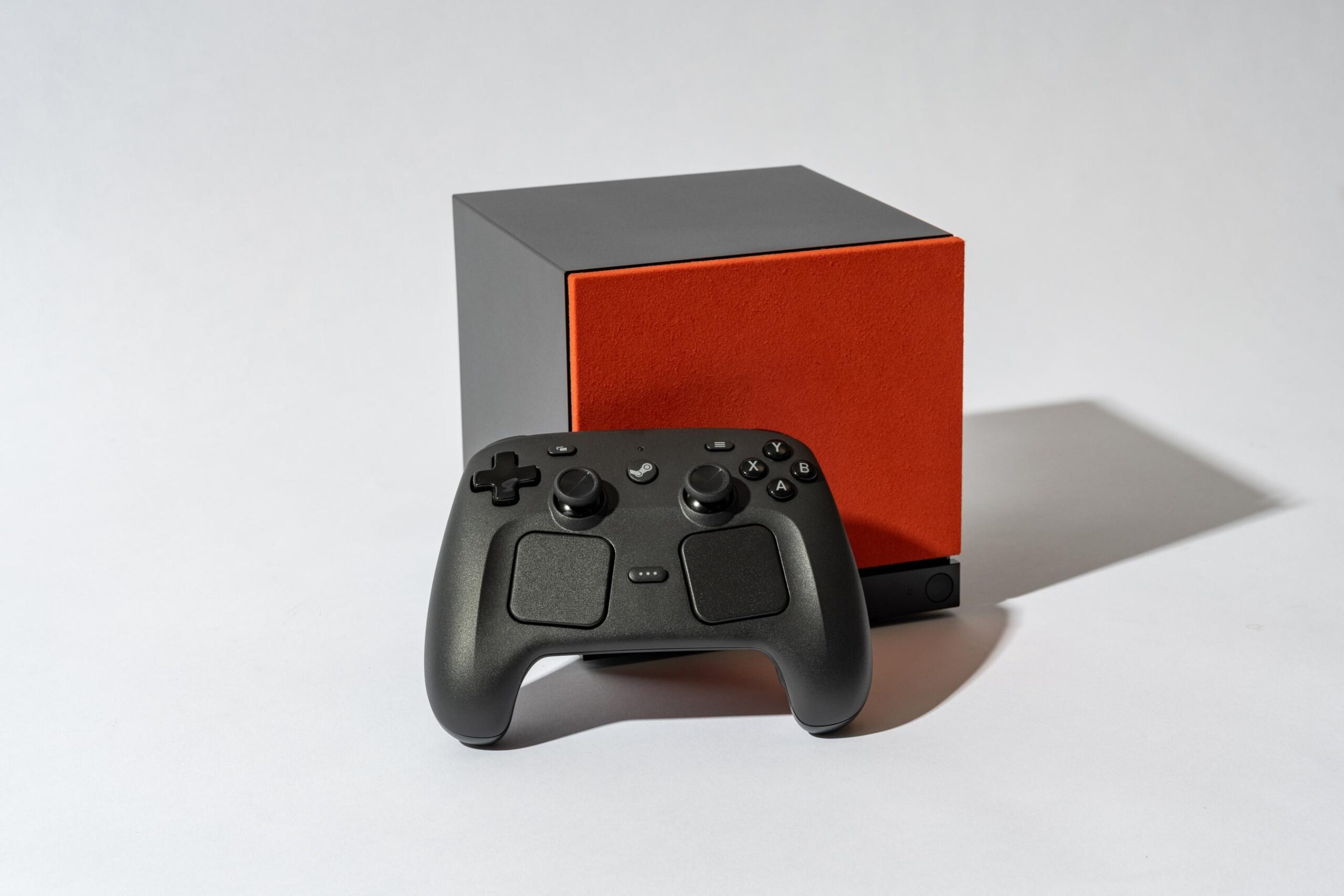 The Steam Machine with a red face plate and the Steam Controller propped up in front of it.