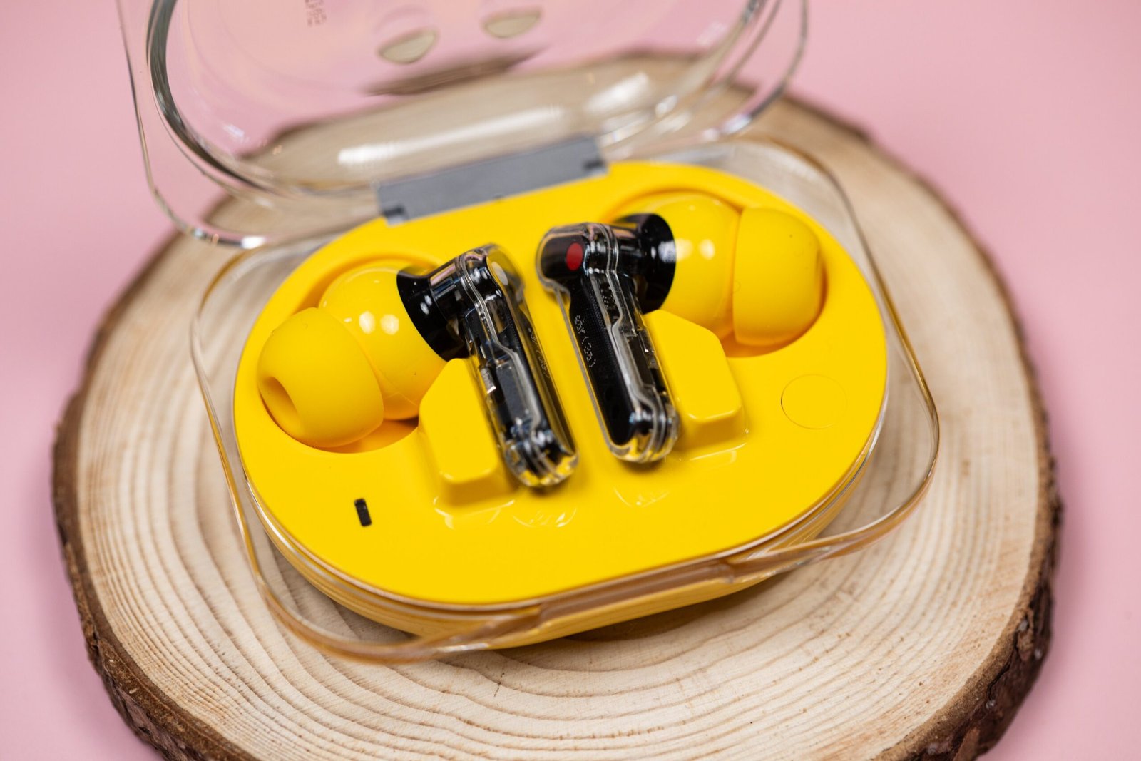 The Nothing Ear 3A earbuds, in yellow, in their open case on a wooden disc with a mauve background.