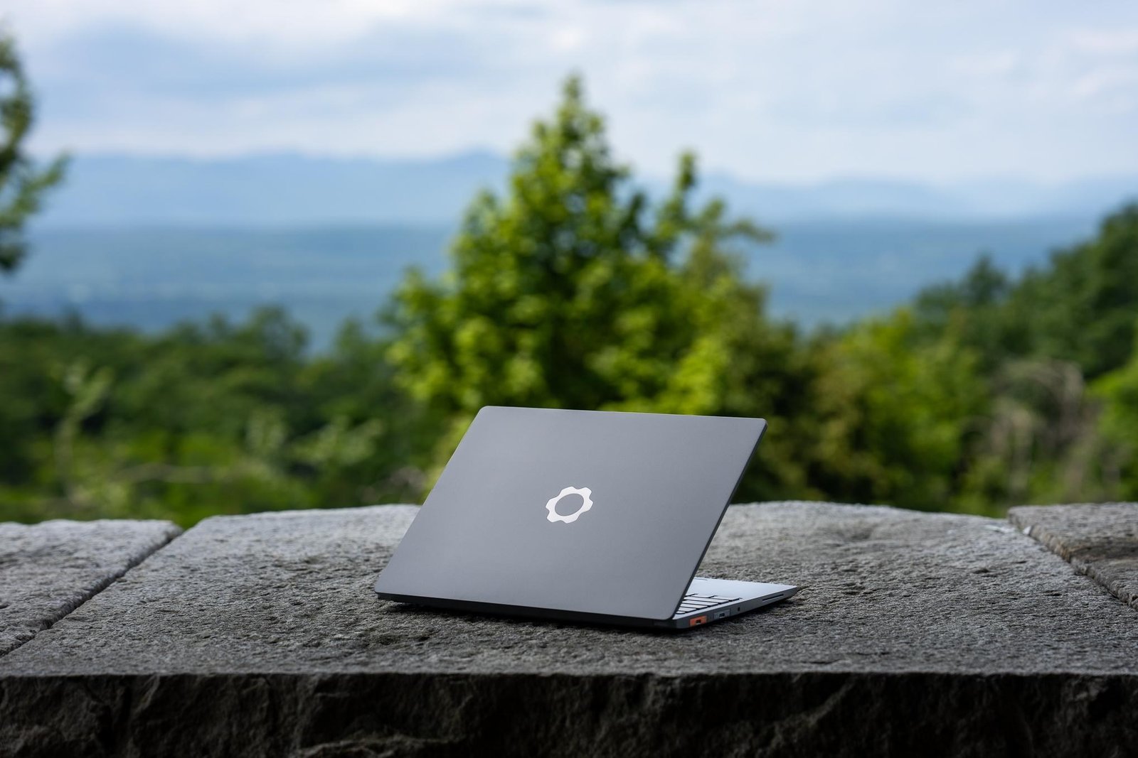 A rear view of the Framework Laptop 13 Pro on a stone slab in front of a tree-filled landscape.