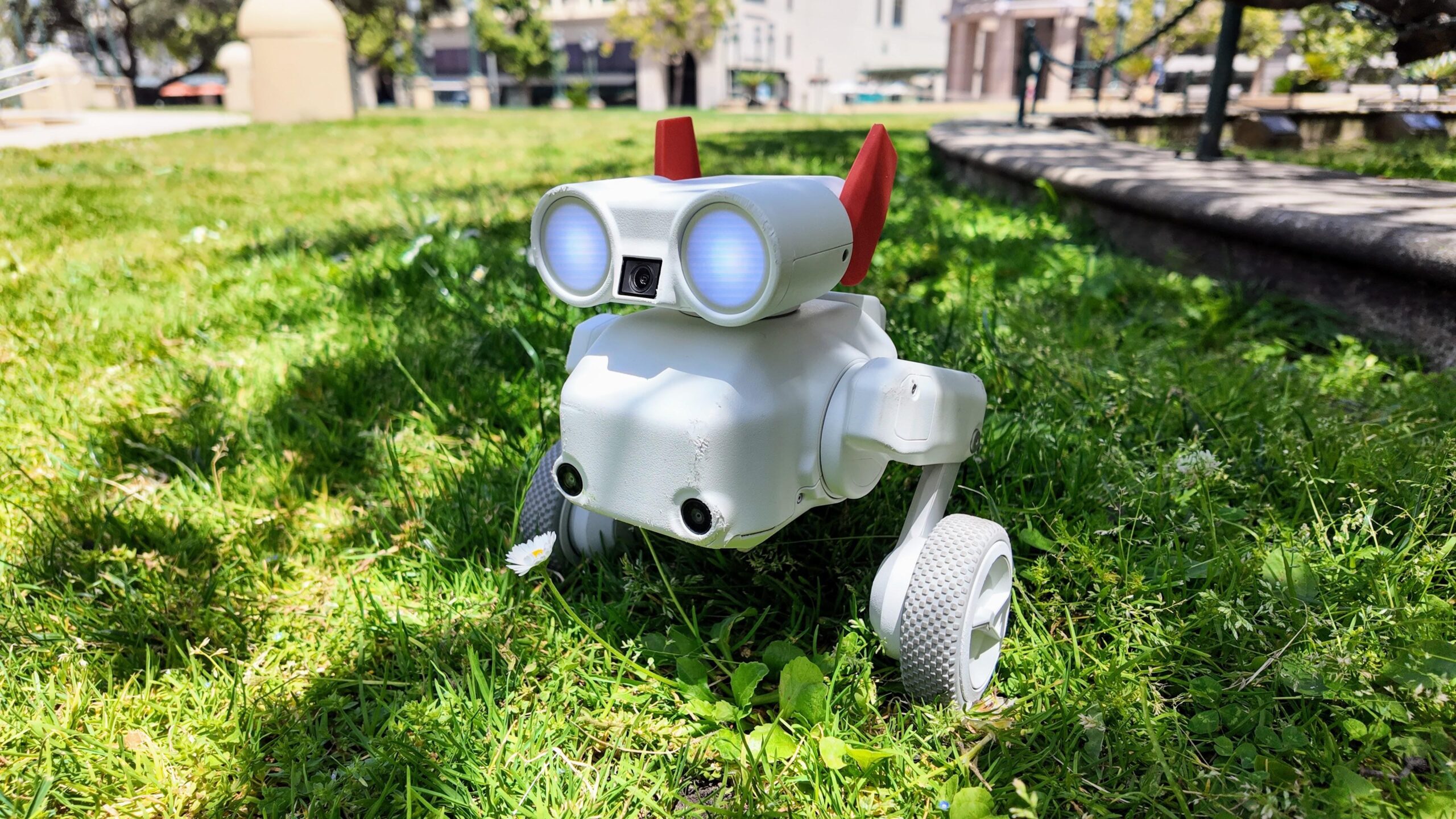 A white two-legged robot, with wheels on the end of each leg, mounted astride a white rectangular prism, with a pair of binocular like eyes on the top, with two orange ears hanging off the back.