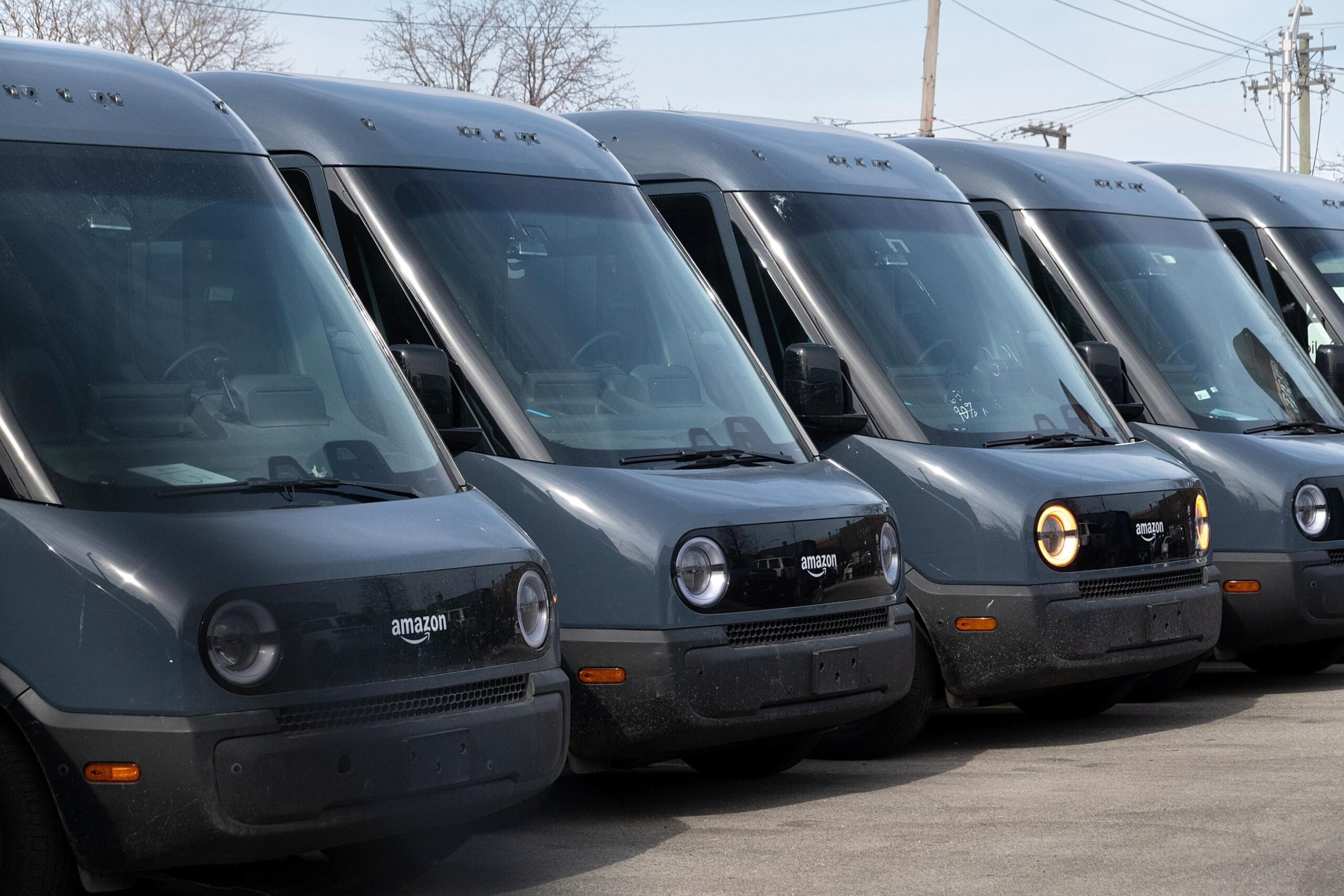 A line of parked dark blue Rivian Amazon branded delivery vans. A line of parked dark blue Rivian Amazon branded delivery vans.