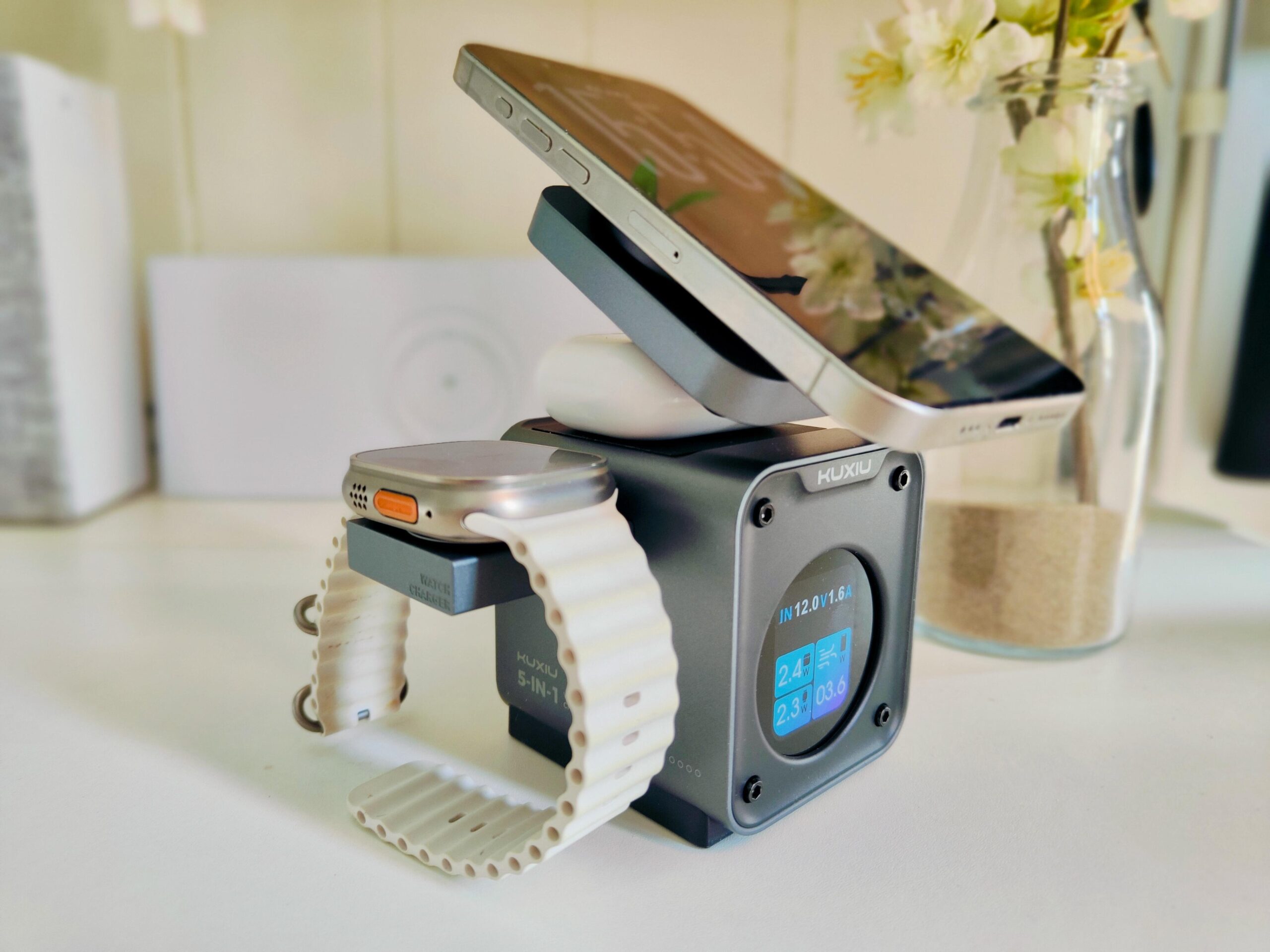 the Kuxiu D5 on a desktop charging an iPhone, Apple Watch Ultra, and AirPods simultaneously, with the respective power draws displayed on the front of the boxy charging dock.