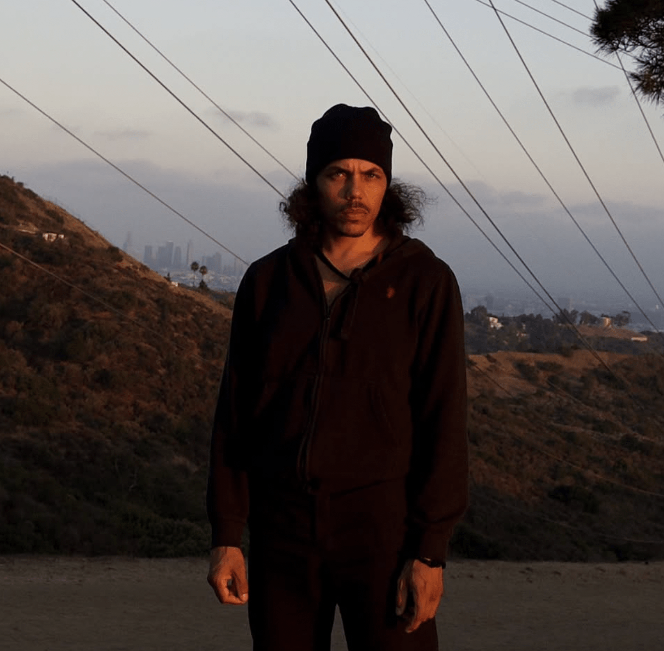 Artist 1010Benja in 2025 standing in a road wearing all black during golden hour.