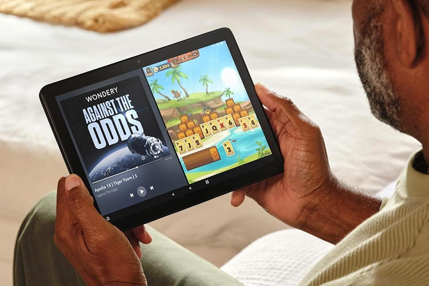 A person holds the Amazon Fire HD 10 tablet in two hands while multi-tasking on screen.