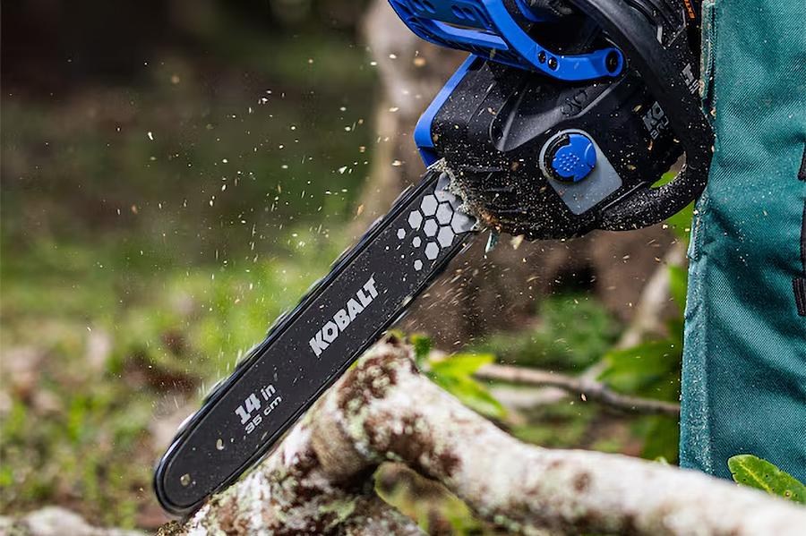 A person saws through a branch using an electric Kobalt chainsaw.