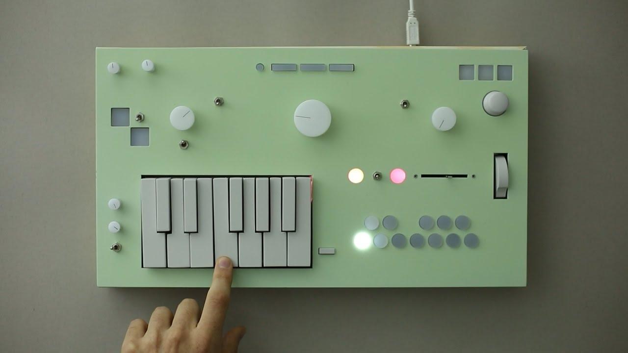 Mint green Nopia synth with it’s odd selection of controls on a plain tabletop being played by a single finger.