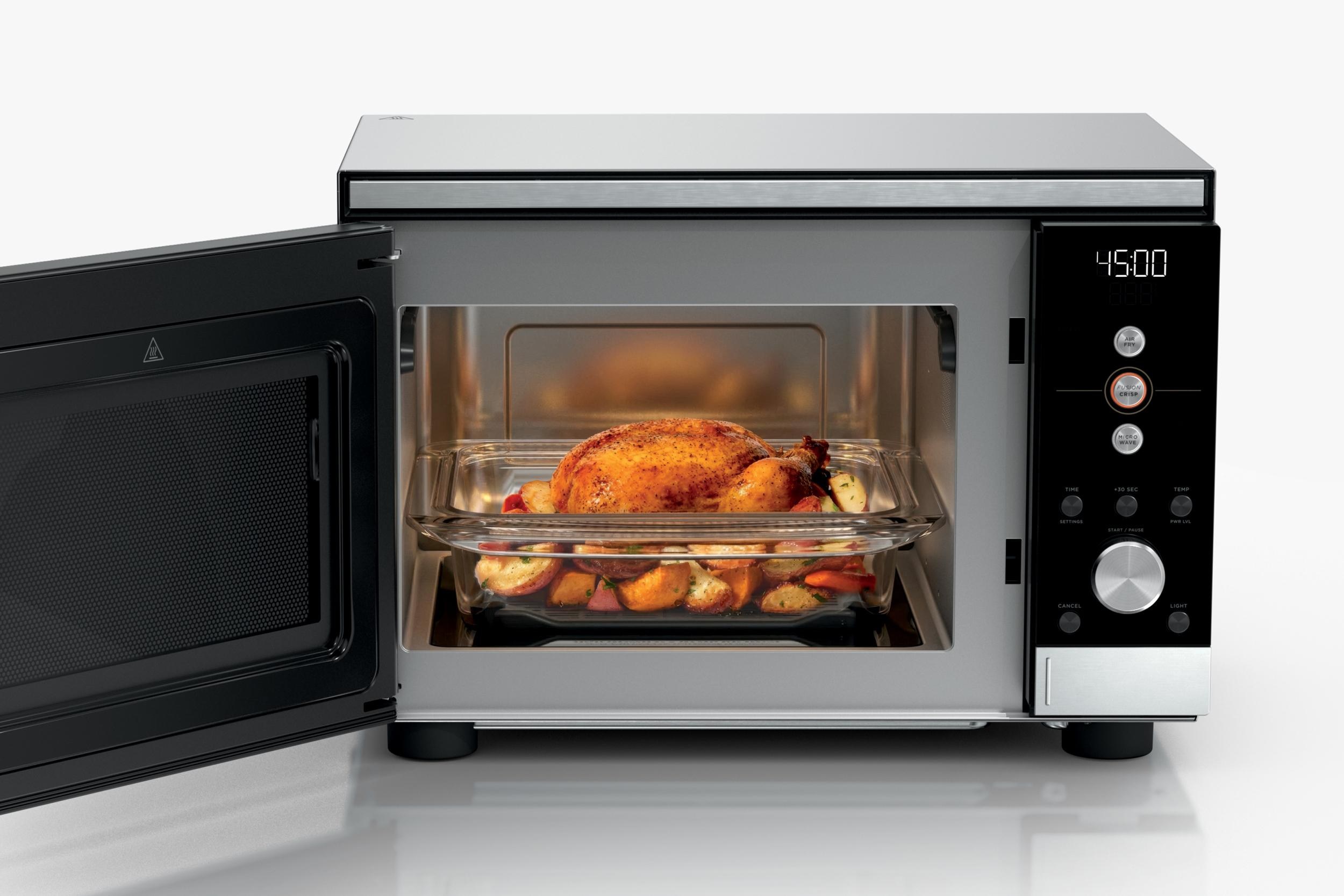 The Ninja Crispi Microwave with its door open and a cooked chicken with vegetables inside.