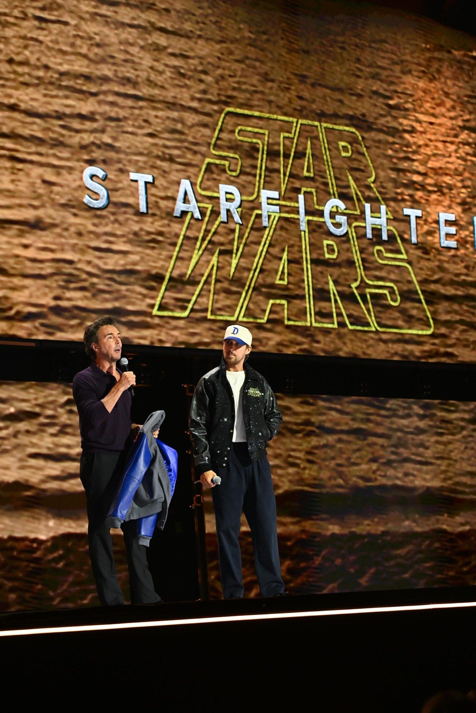 Ryan Gosling and Shawn Levy in front of a Star Wars Starfighter logo.
