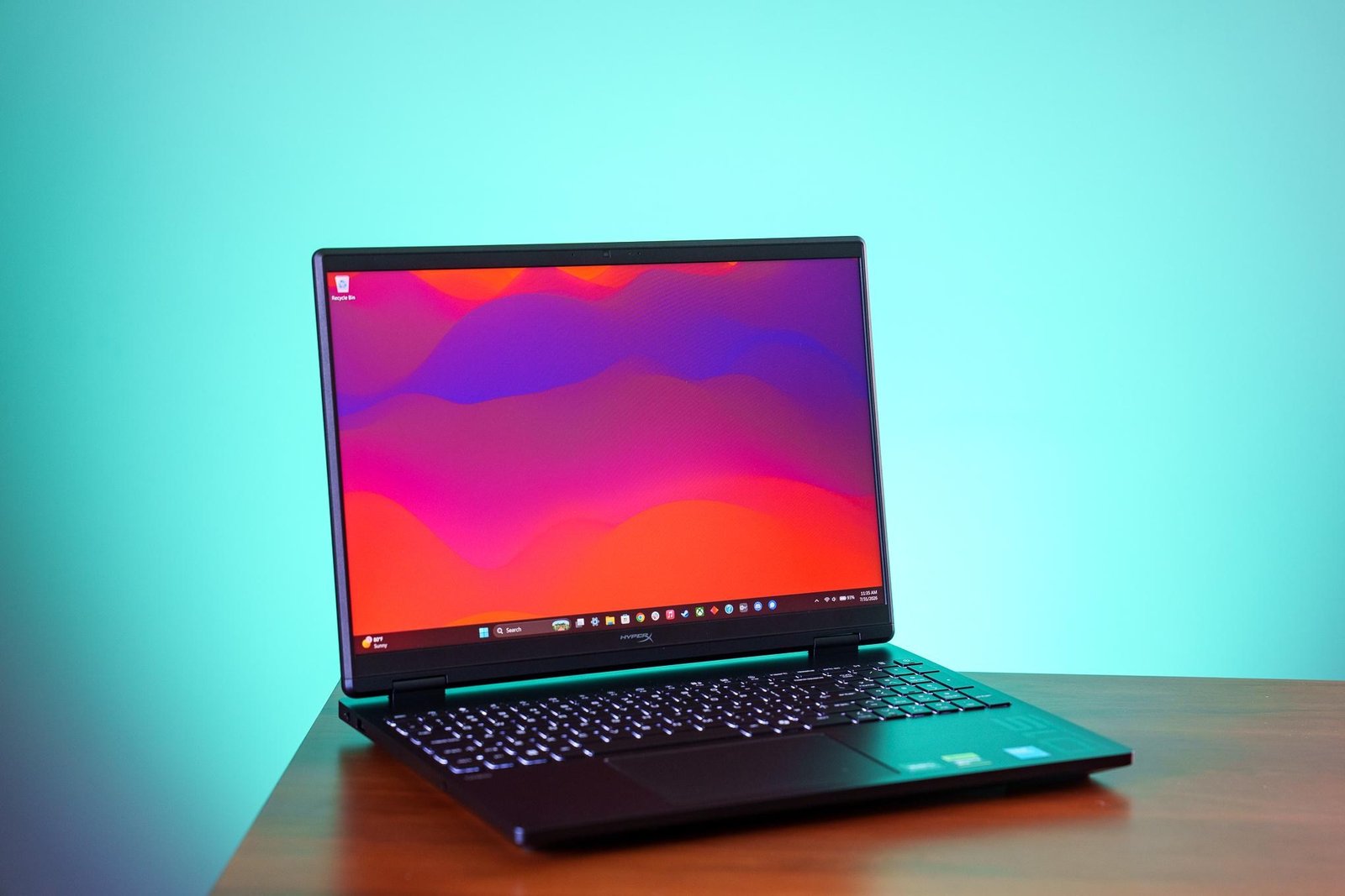 A HyperX Omen 15 gaming laptop on a wood table, in front of a splash of cyan colored light.