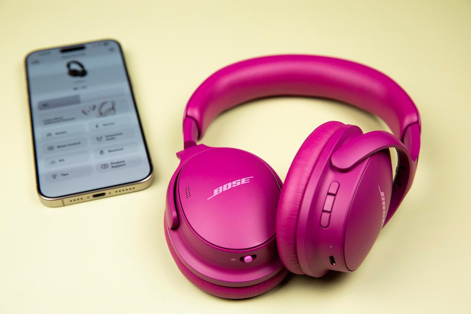 Gen 2 Bose QuietComfort Headphones sitting on a pale yellow surface next to a iPhone.