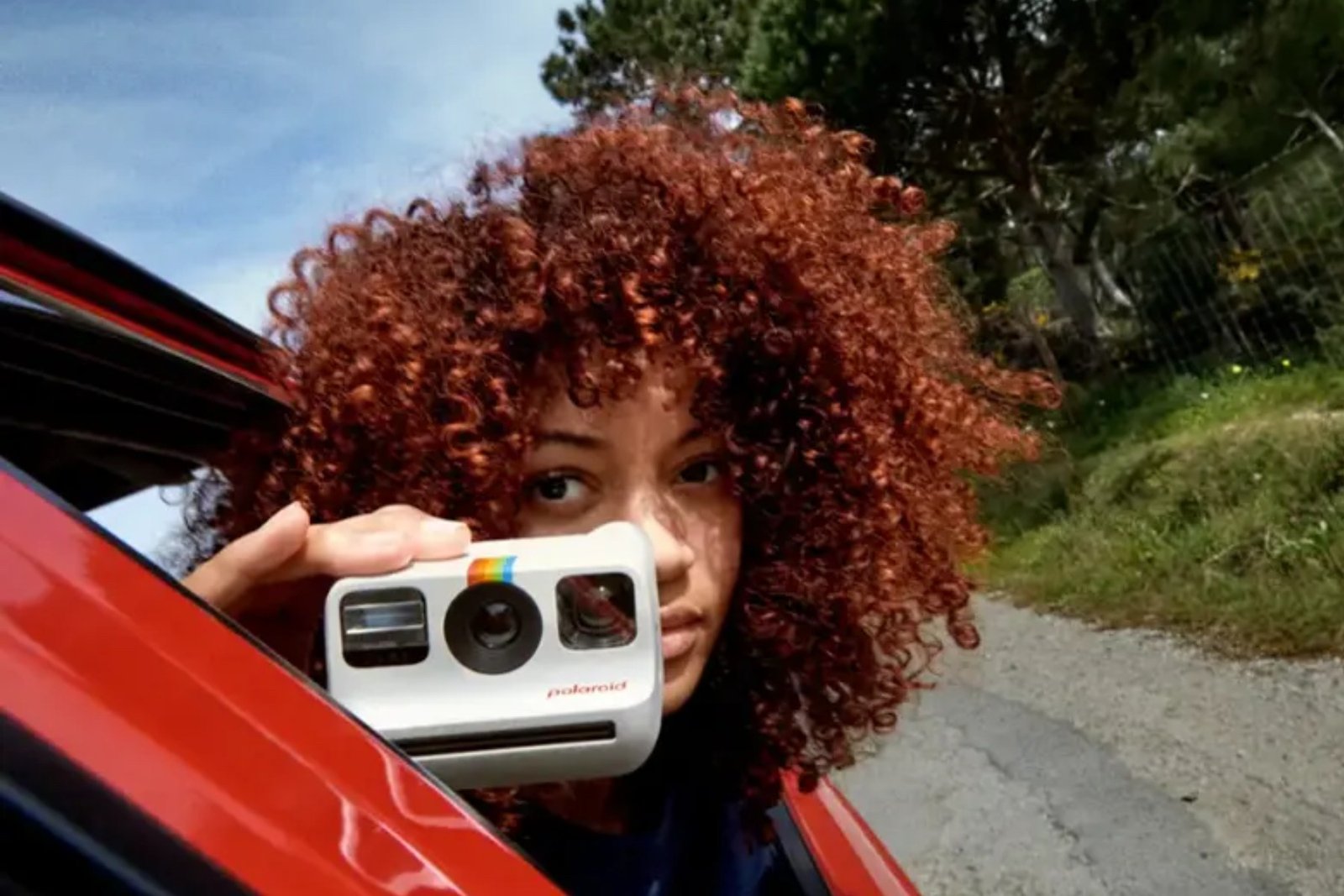 A woman in a car holding a Polaroid Go Generation 2 Instant Camera.