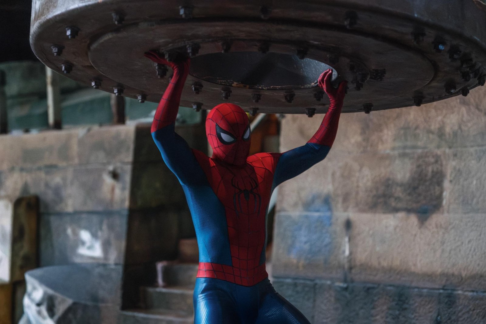 Spider-Man holding up a large, heavy metal object over his head.