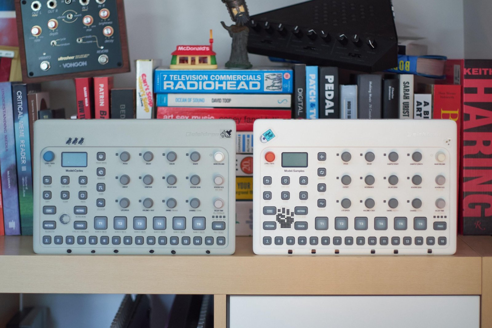 The Elektron Model:Cycles and Model:Samples grooveboxes on a shelf in front of books, a cassette player, and other random nonseense.
