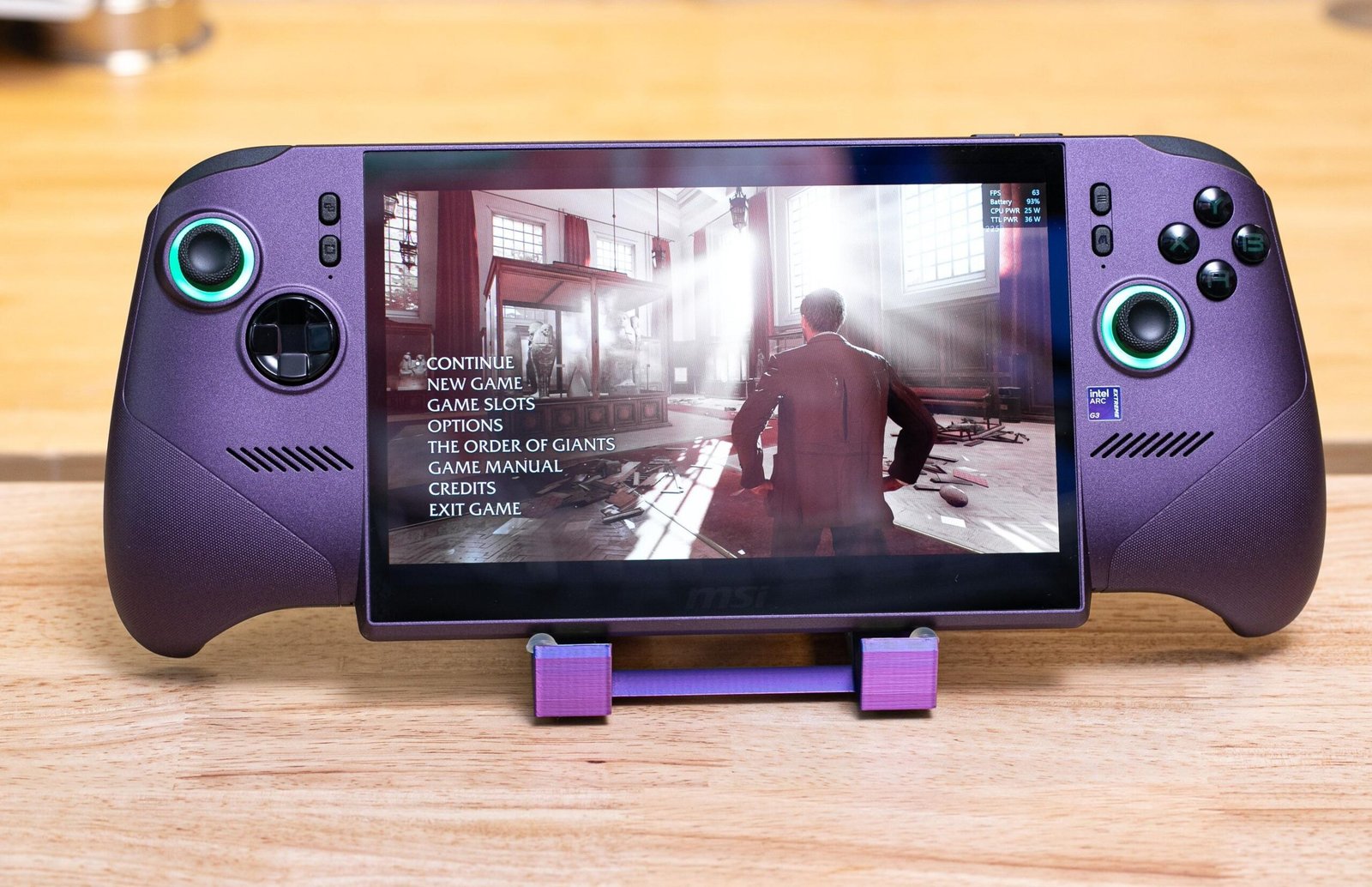 A purple handheld with lit-up joysticks and the intensive Indiana Jones game on screen, facing the camera, on a purple 3D-printed stand.