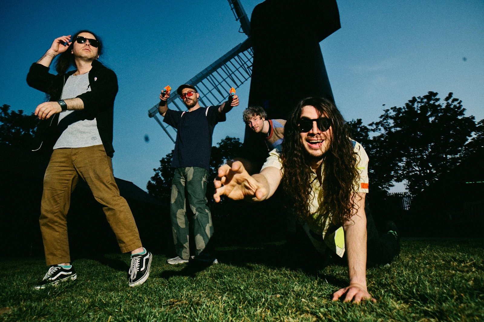 A band photo of Anamanaguchi on a grass field in front of a windmill.
