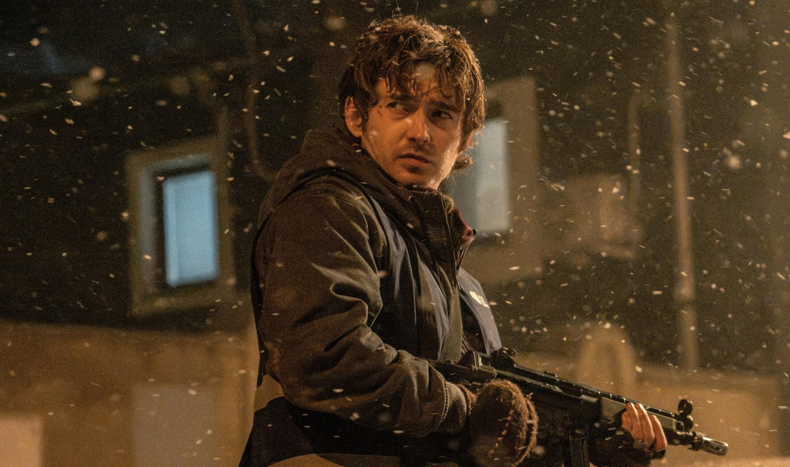 A man in winter clothing standing in the middle of a city street while holding a gun.