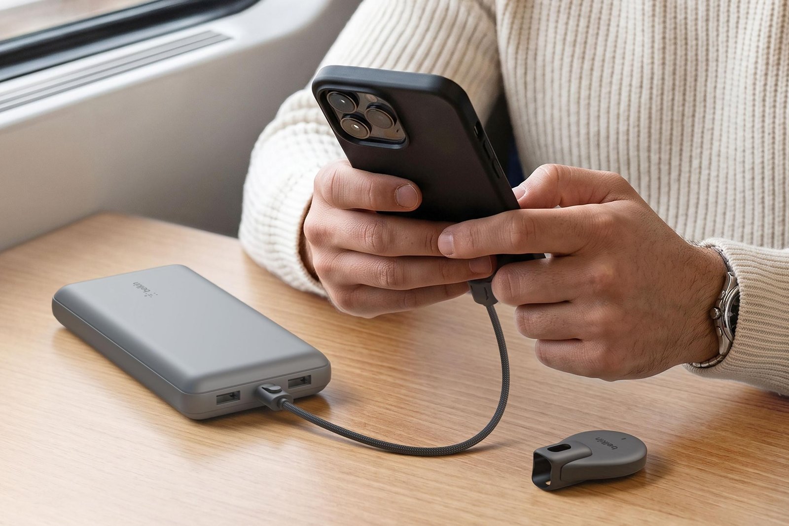 A person uses a smartphone connected to a power bank with a short USB-C cable.