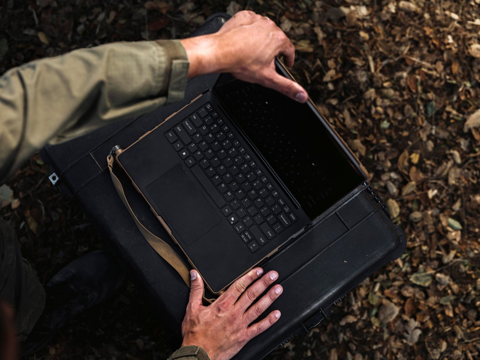 A person dressed in military fatigues using a rugged BlueChip laptop placed on a hard case.