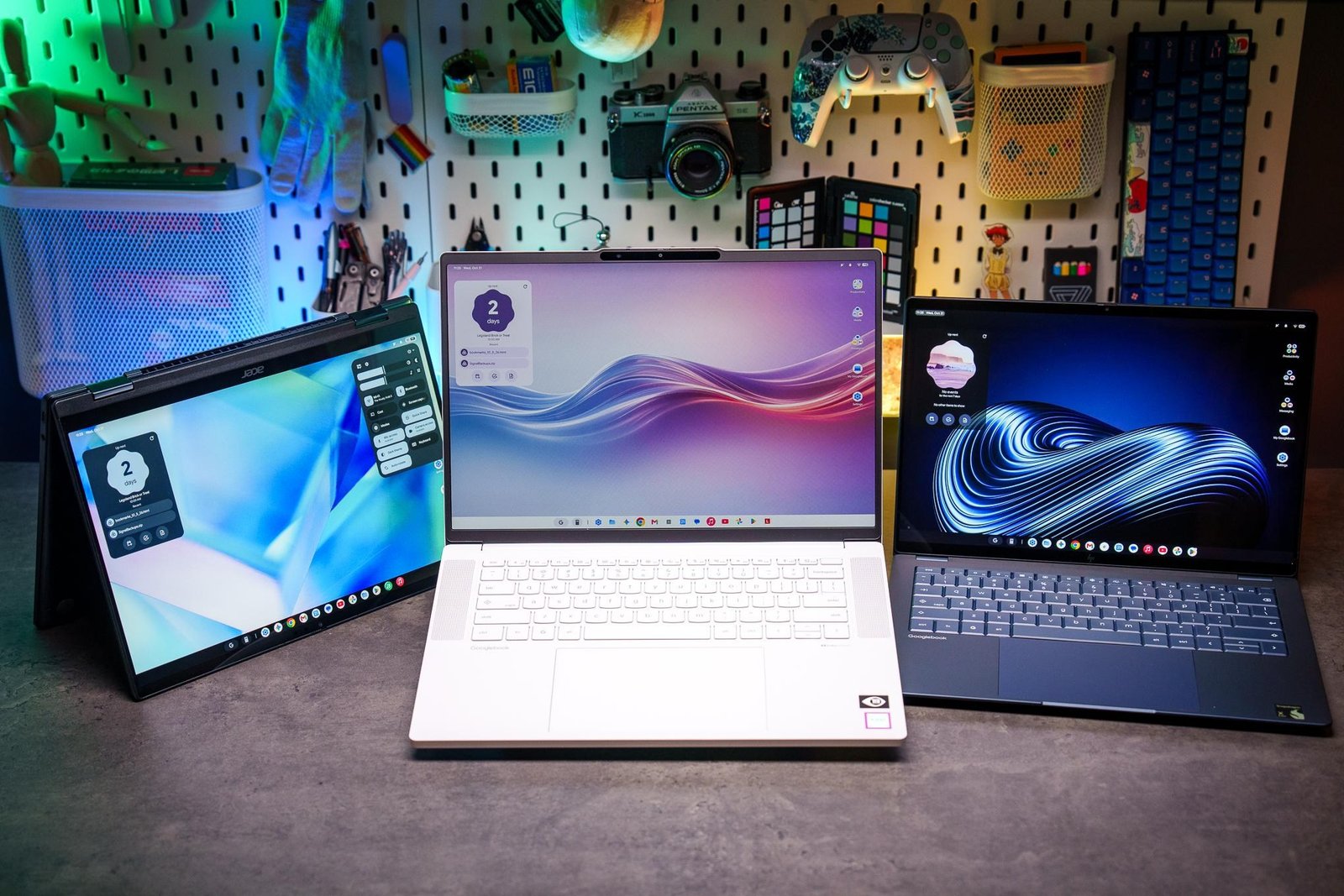 A lineup of three Googlebooks (left to right: Acer Googlebook 14, Lenovo Googlebook 15, and HP Googlebook 14) in front of a colorfully lit background.