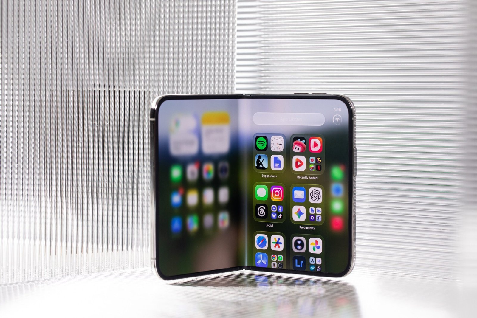 The iPhone Duo propped open like a book. The left side of the display is blurry from the transition, while the right side shows rows of apps.