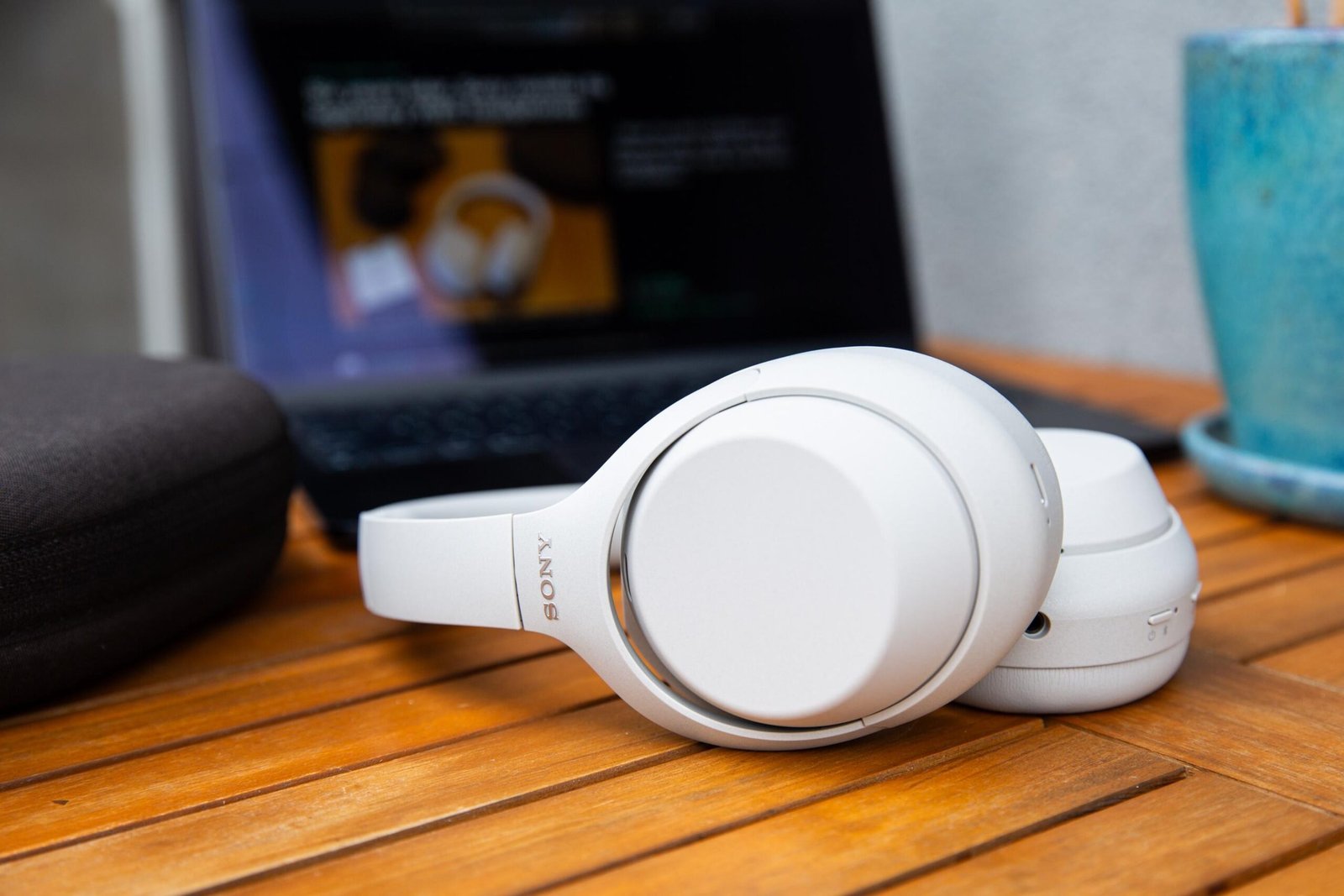 The Sony XM4C headphones on a wooden table in front of their case and a MacBook.