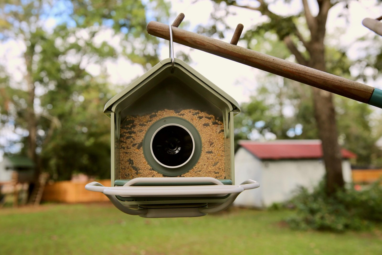 A bird feeder hanging on a pole in a garden.