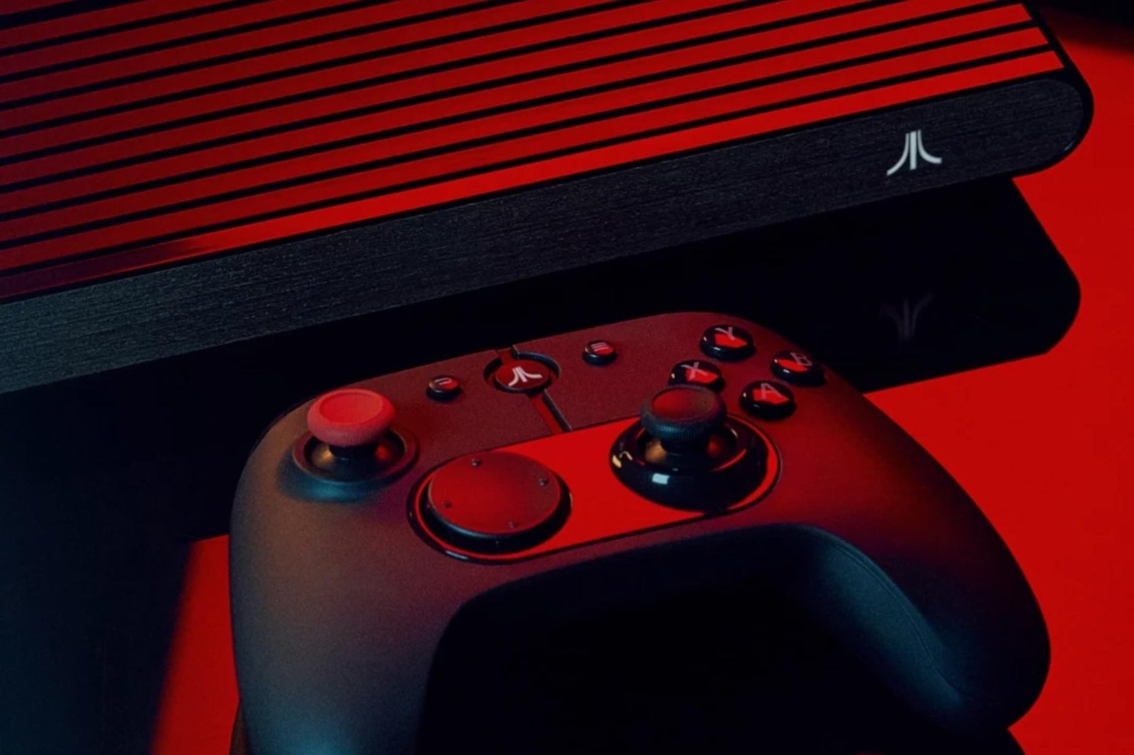A close-up of a controller next to the Atari VCS retro console bathed in red light.