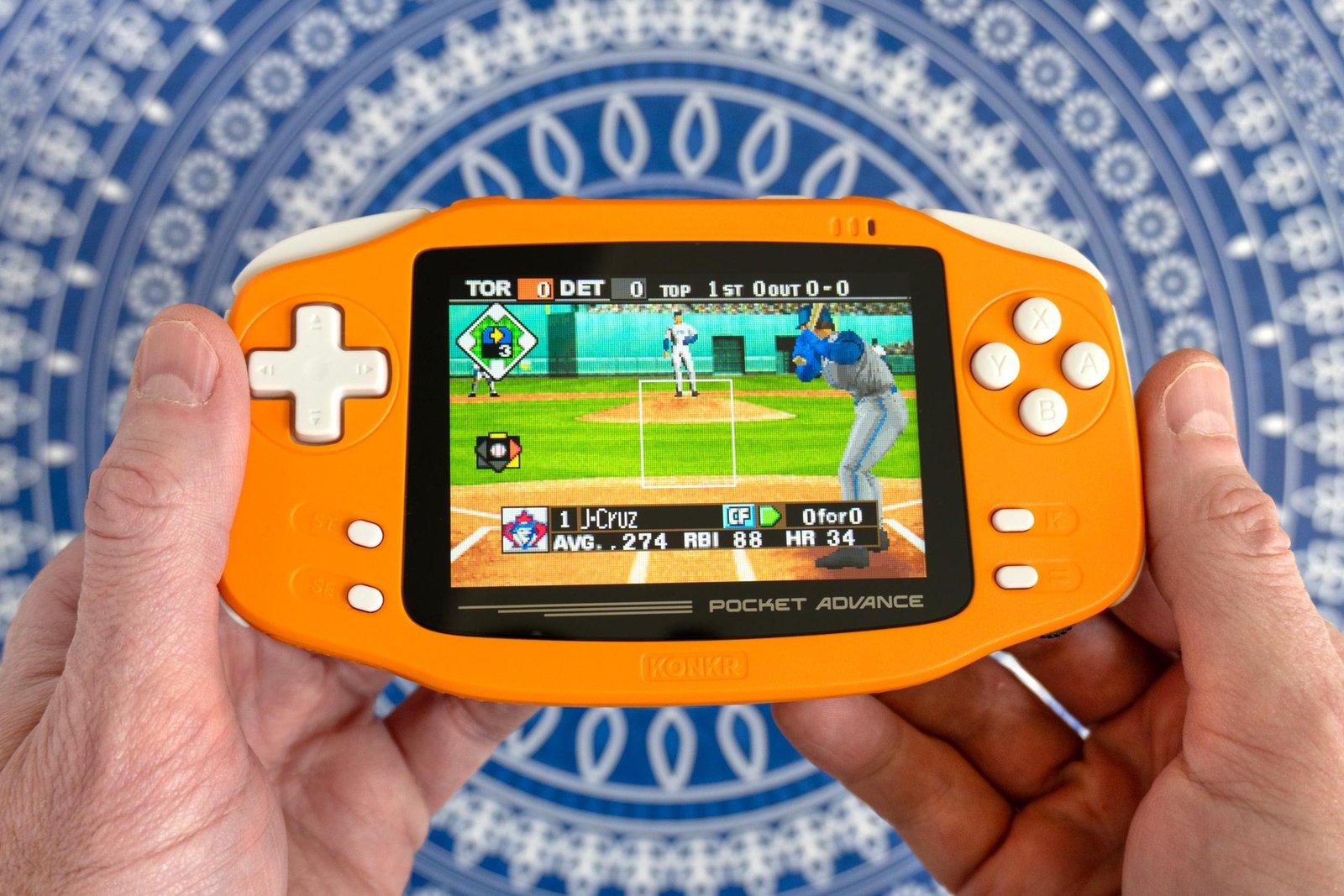 A person holds the Ayaneo Konkr Pocket Advance in two hands with a baseball game shown onscreen.