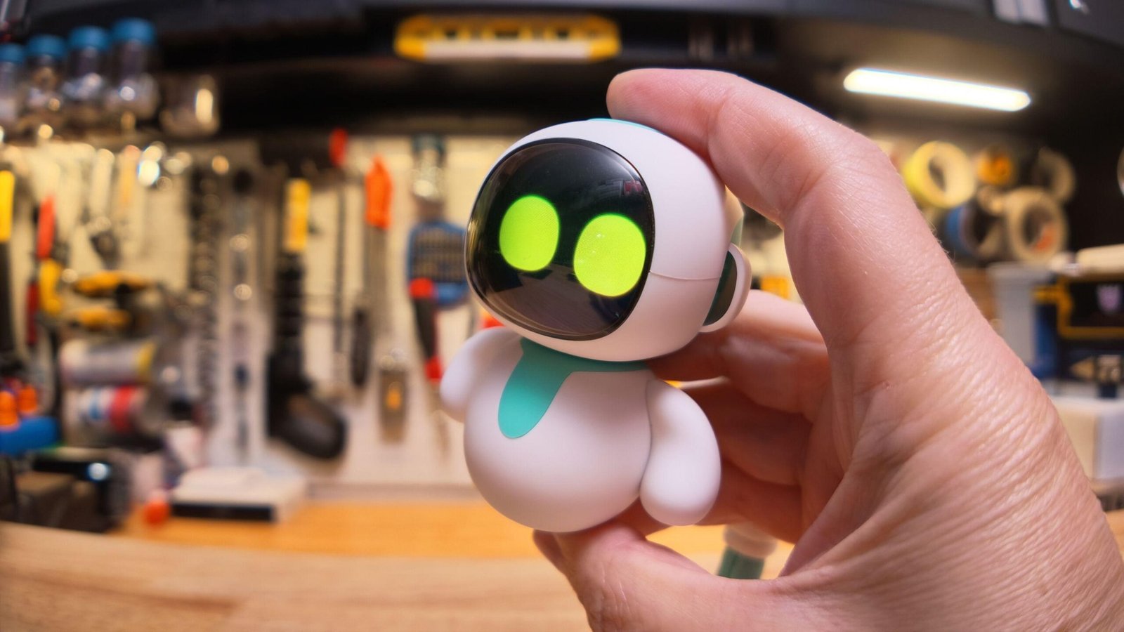 Holding an Eiliko robot toy between my thumb and forefinger in front of my workbench.