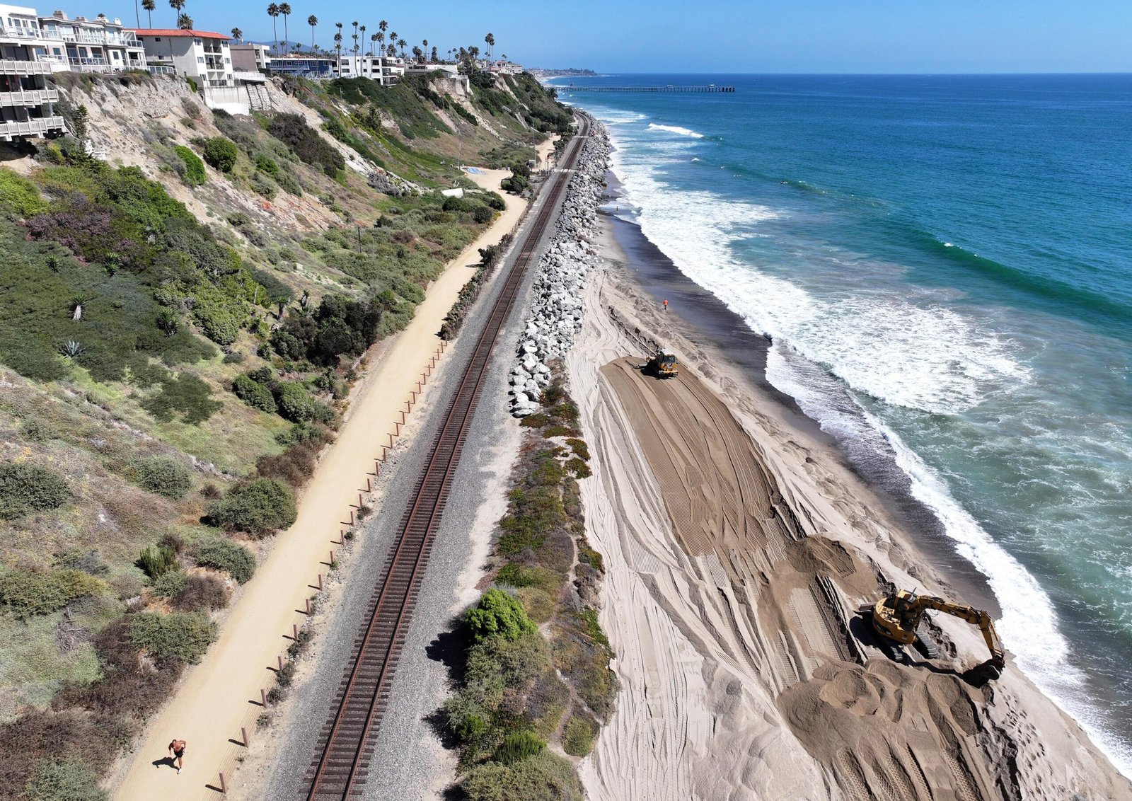 An aerial view of equipment moving fresh sand as a jogger passes.