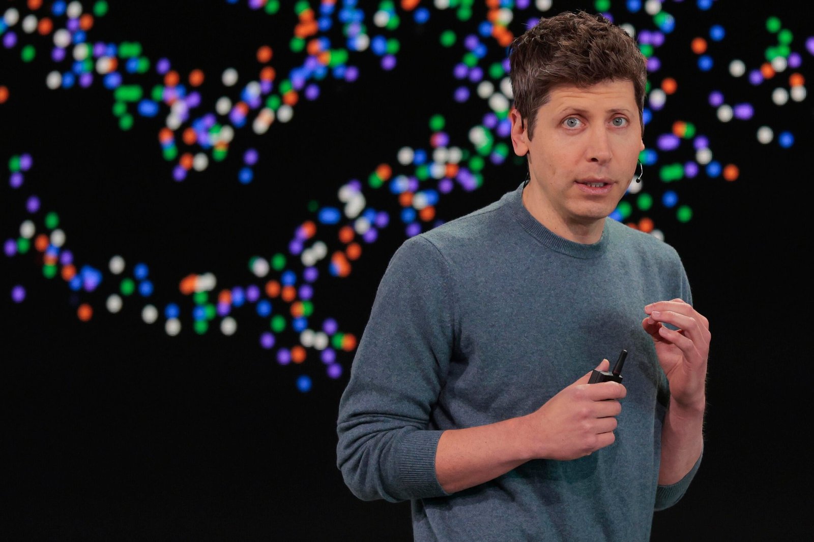 Sam Altman speaking in front of OpenAI logo