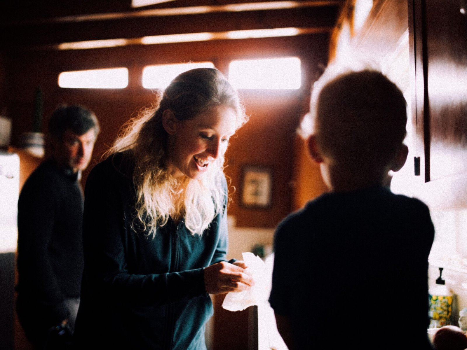 Elizabeth Holmes is talking to her child. In the background, Nathan Fielder lurks, watching.