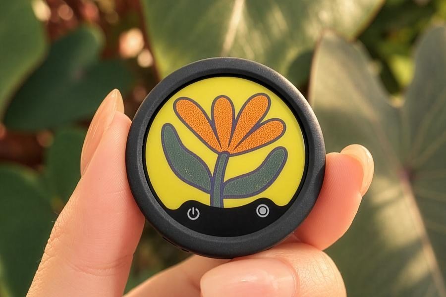 A person holds the Insta360 Mic wireless transmitter between two fingers with a flower illustration displayed on its screen.