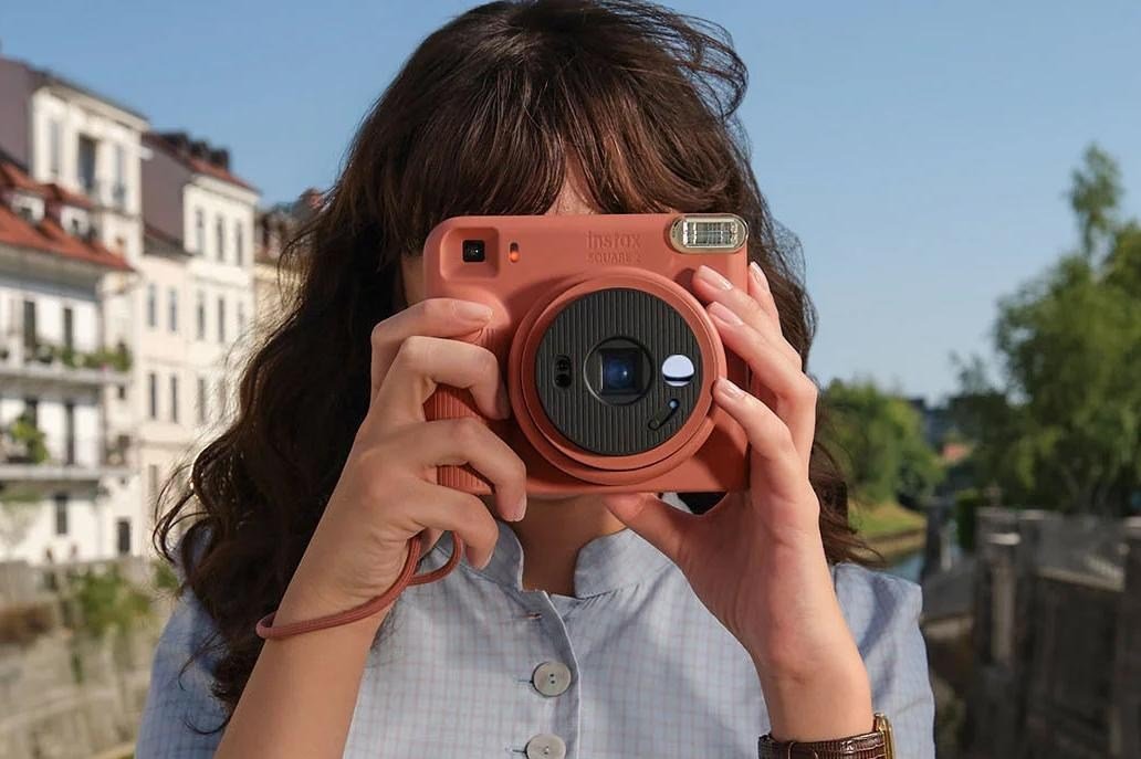 A person holds the Fujifilm Instax Square 2 up to their face while taking a photo.