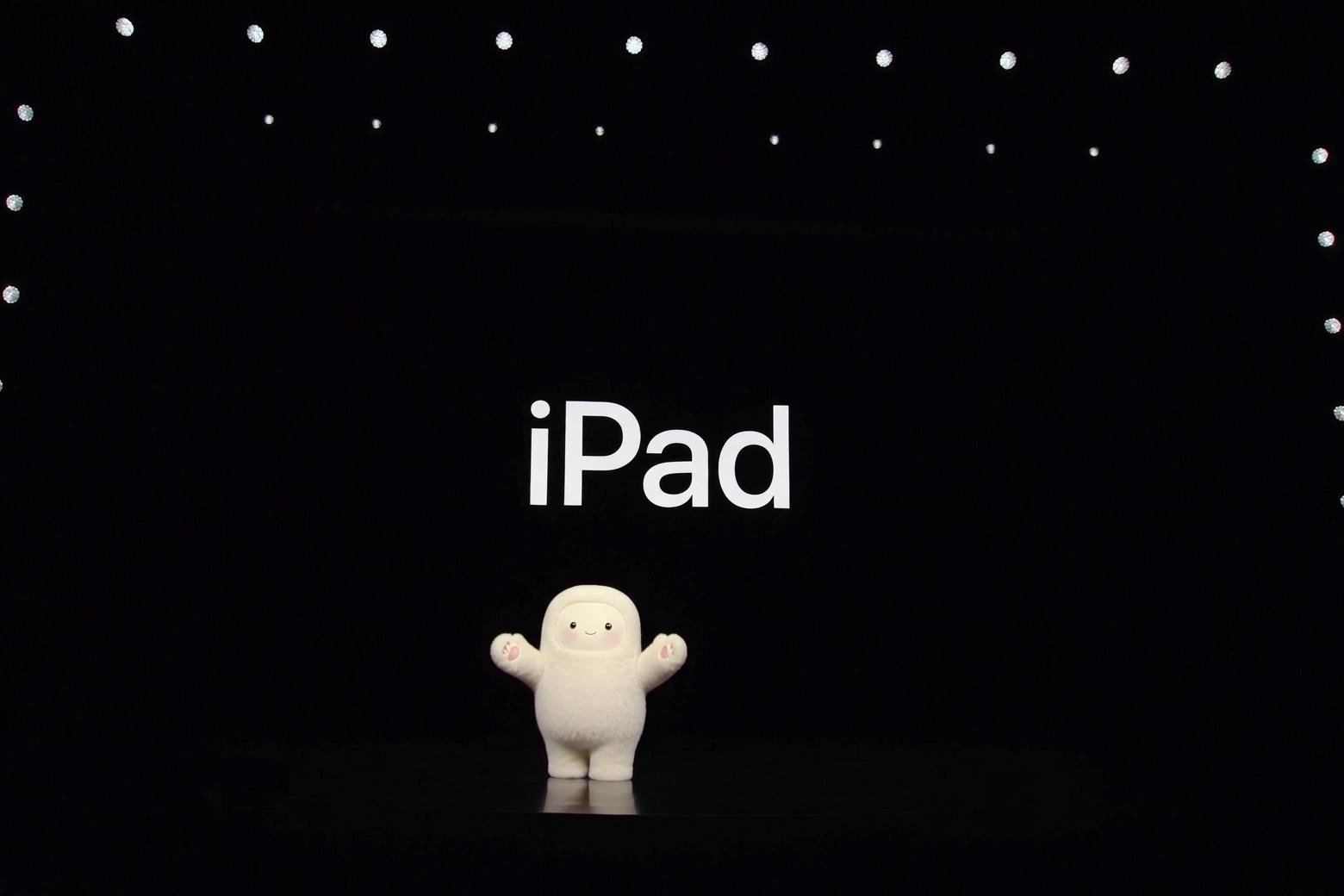 The Meta Muse mascot standing on a stage surrounded by lights with the word iPad on screen behind it.